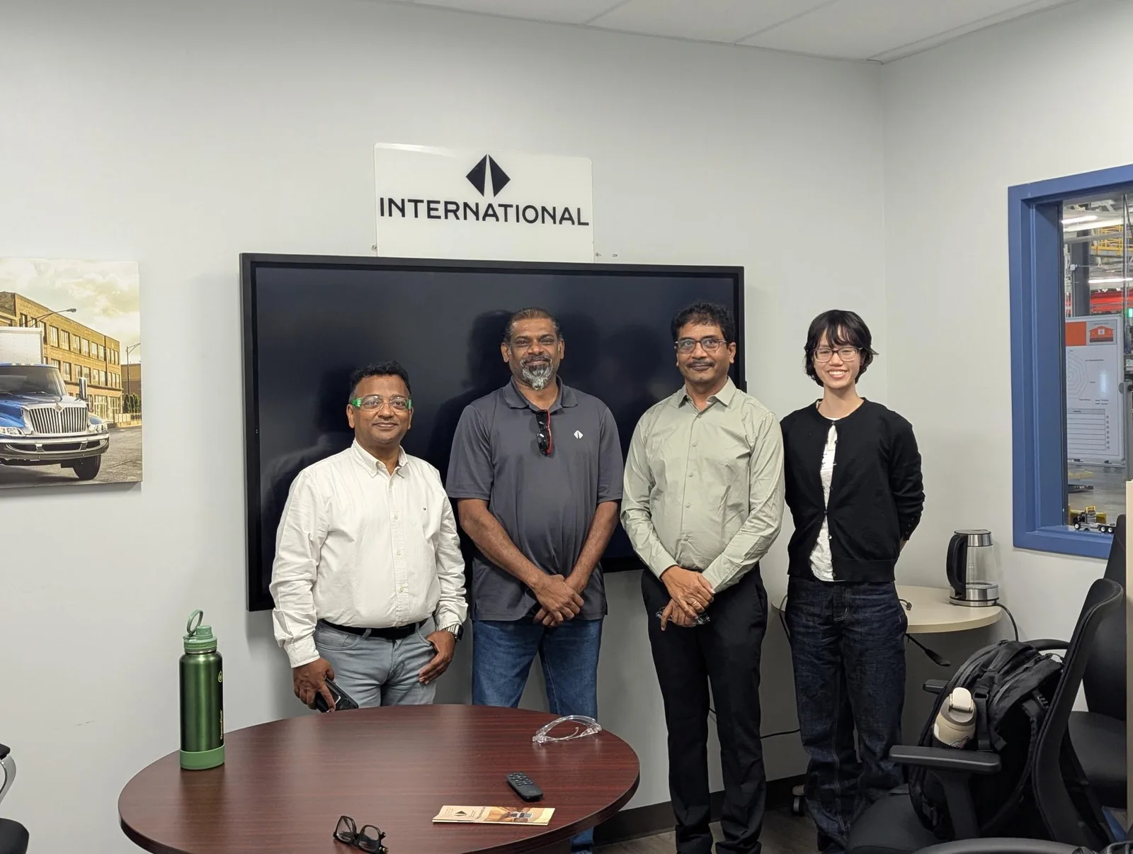 Four people standing together in a plant meeting room