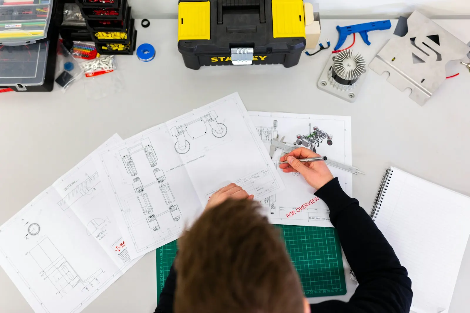 Engineering drawings spread across a desk, someone marking one up